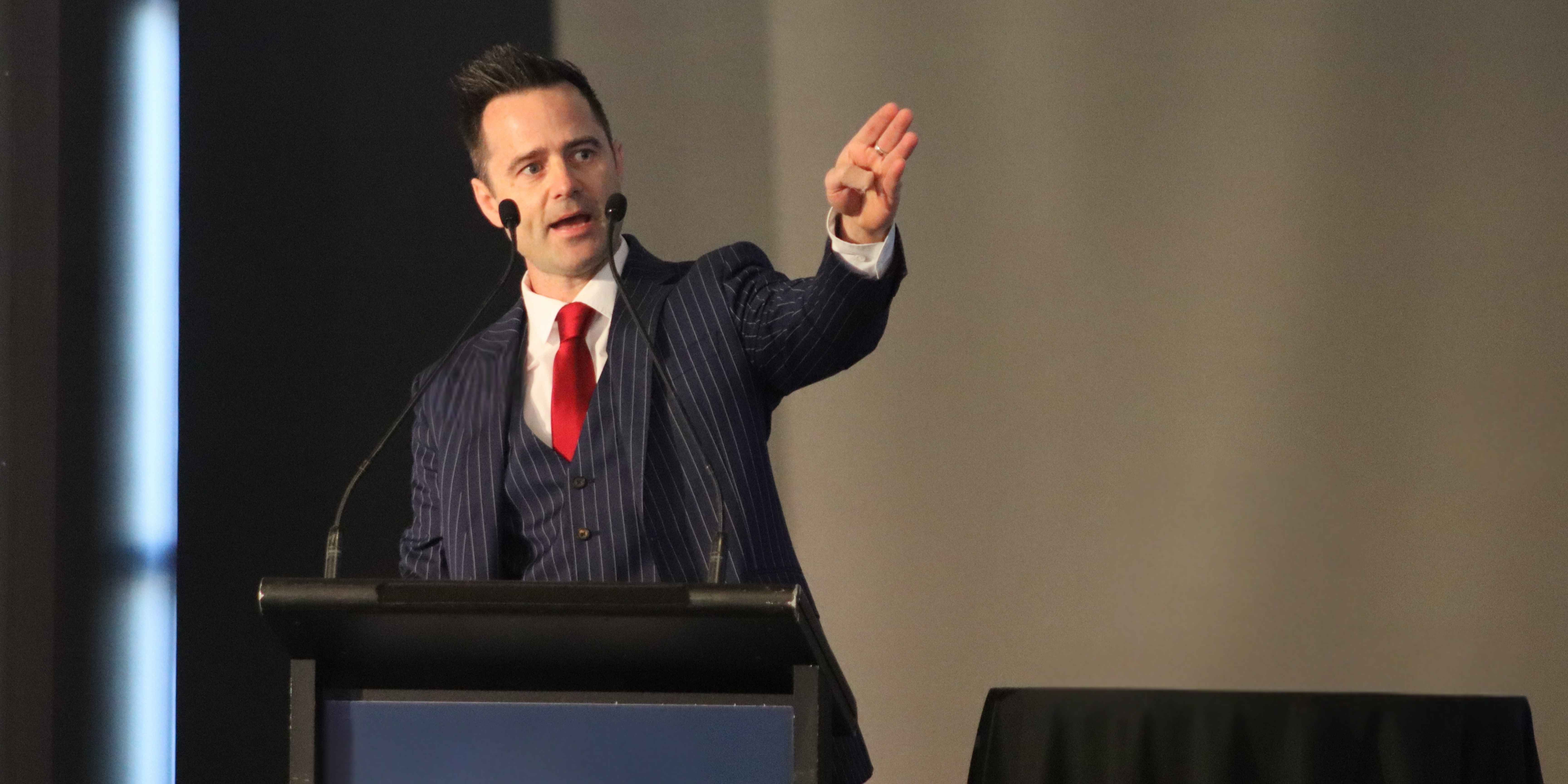 Sam Osborne speaking on stage about conflict transformation through the Demartini Method